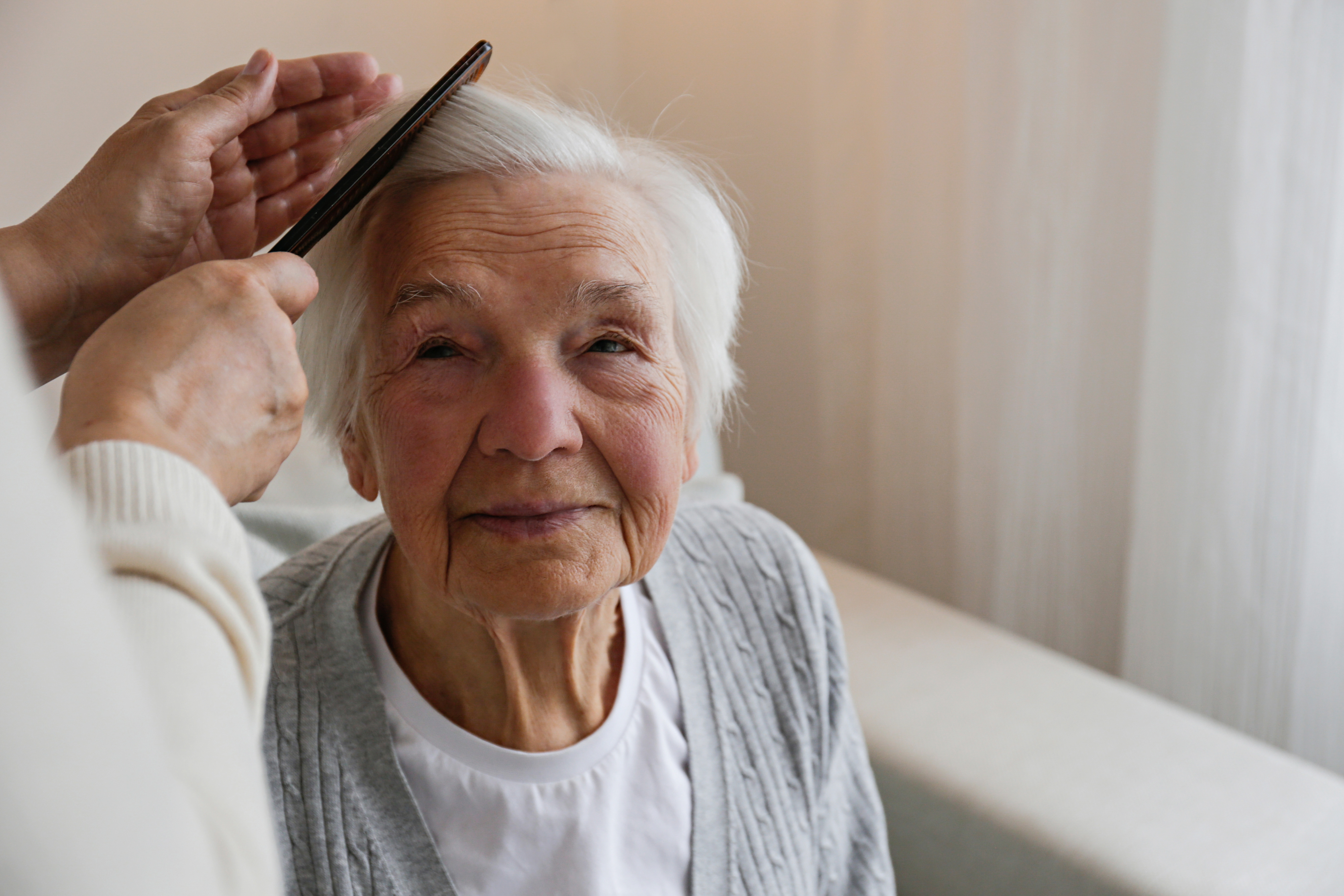 Elderly woman having hair brushed by carer