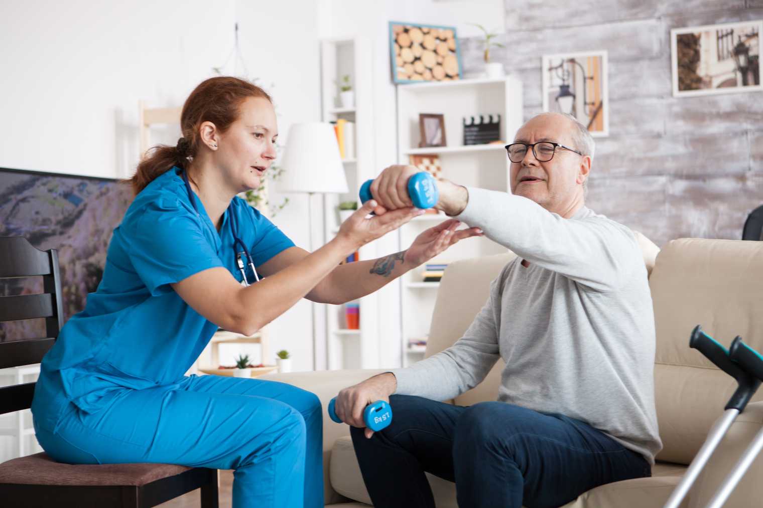 Home care nurse supporting an elderly man lifting a weight