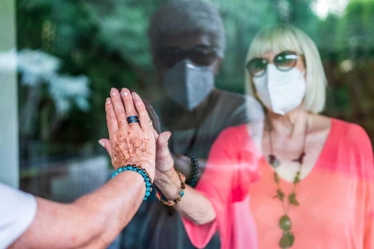 woman isolating in a care home because of covid-19, two women connect through a window as they wear facemasks