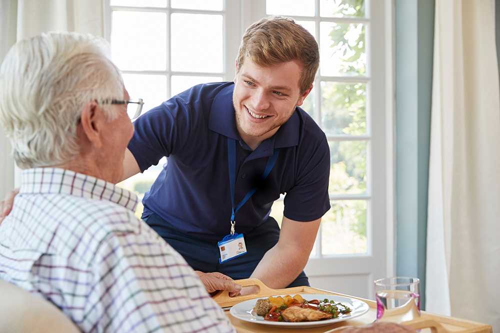 Criteria for going into a care home young guy giving roast dinner to old man