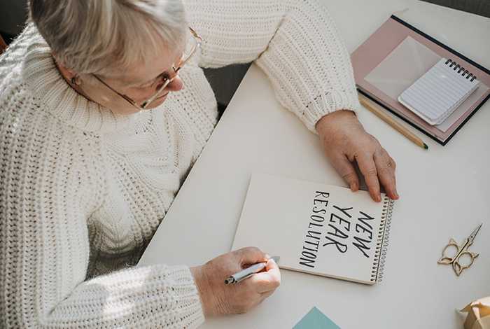 Senior woman writing 'New Year Resolution' on a notepad