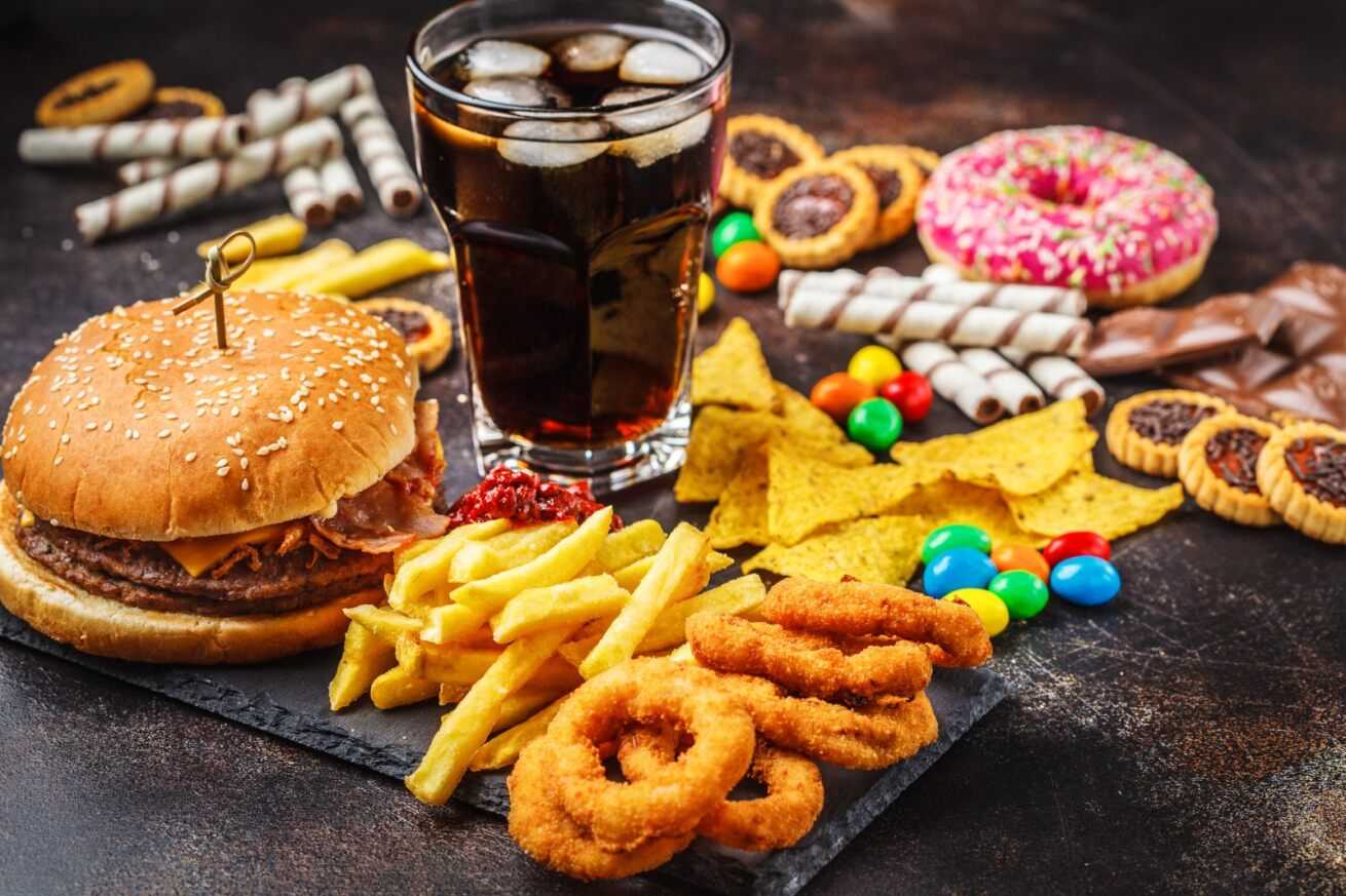 ultra processed foods, fizzy coca cola with onion rings, fries, donuts and sweets, fast food that can cause inflammation
