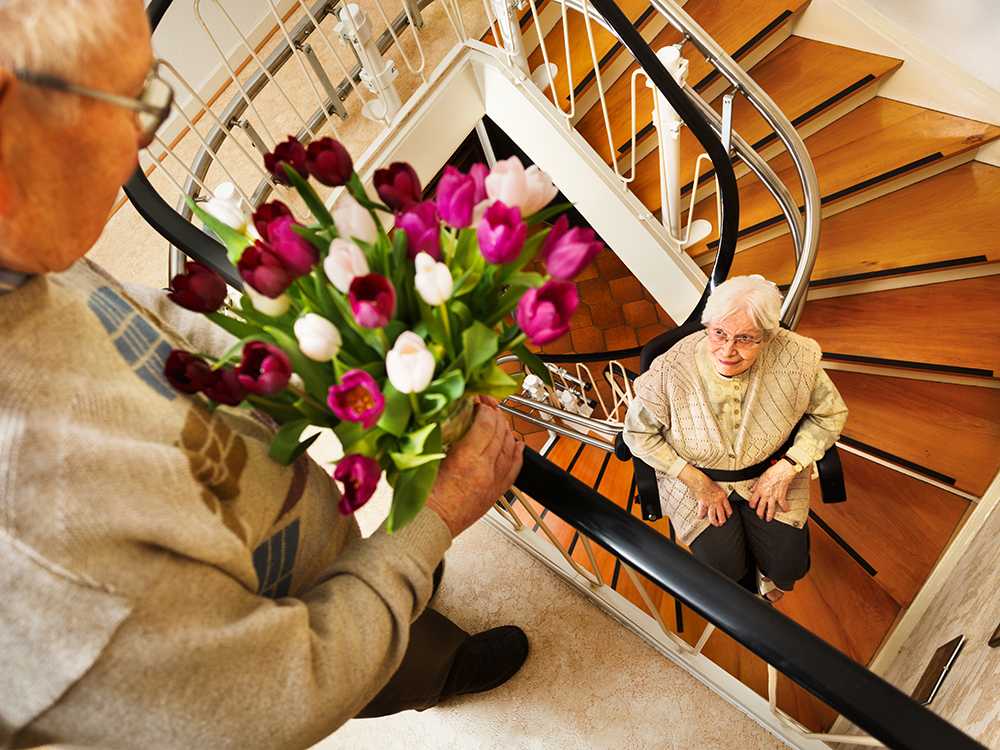 Home adaptations for elderly people. Old man with flowers awaits elderly lady coming up stairs
