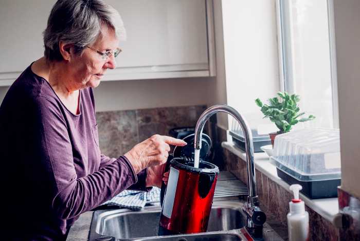 Older woman filling up kettle at the sink