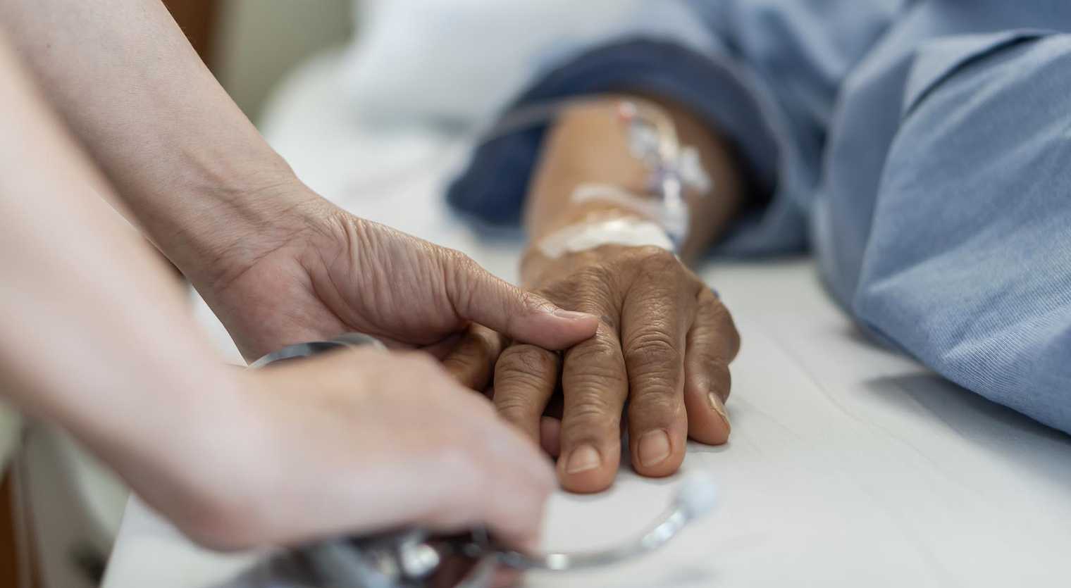 Close up of a doctor's hand holding the hand of an older person