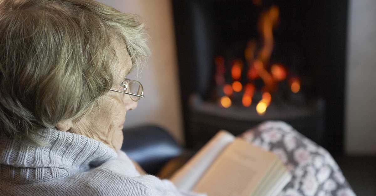 Senior woman reading a book by a fireplace