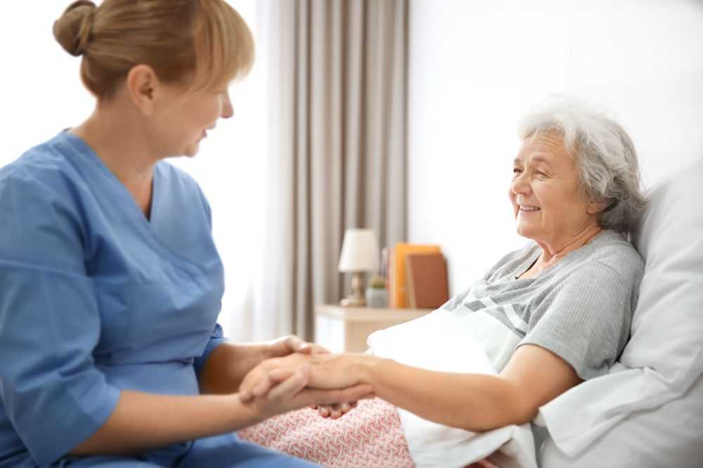 A carer sits with an elderly patient while providing residential respite care